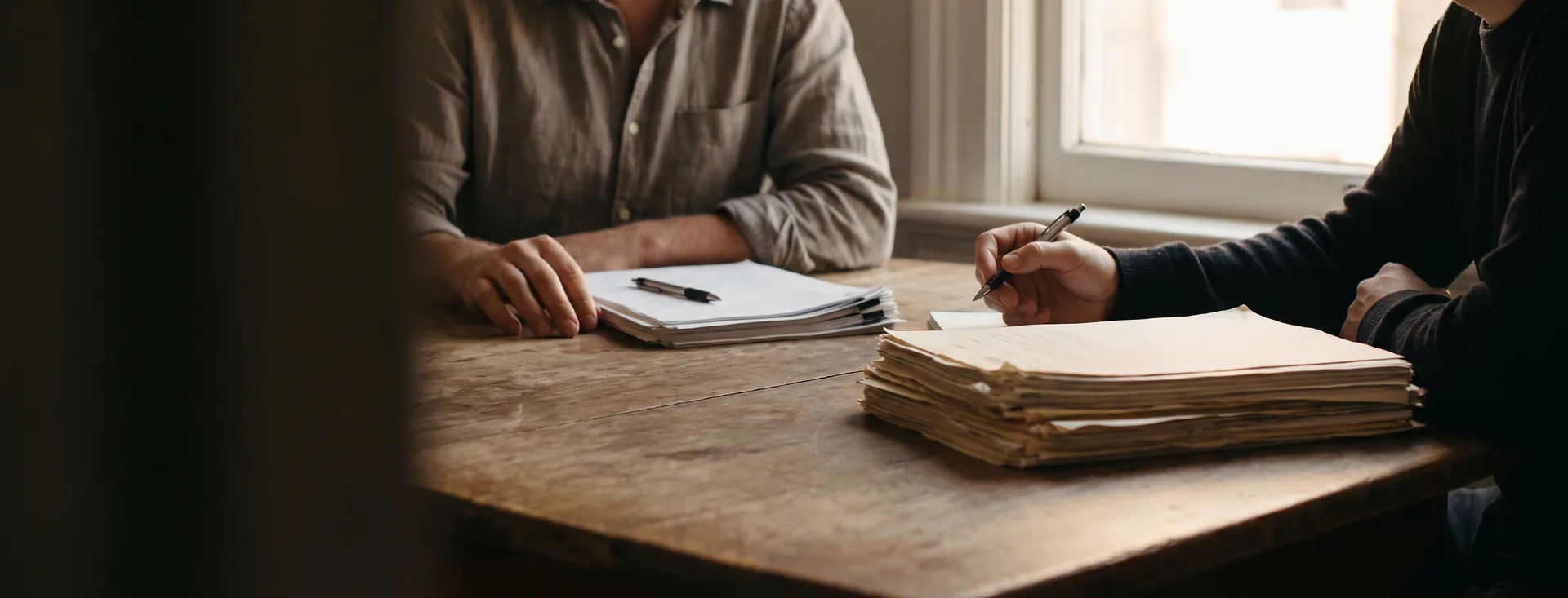 Two people at a table with separate document sets and separate pens
